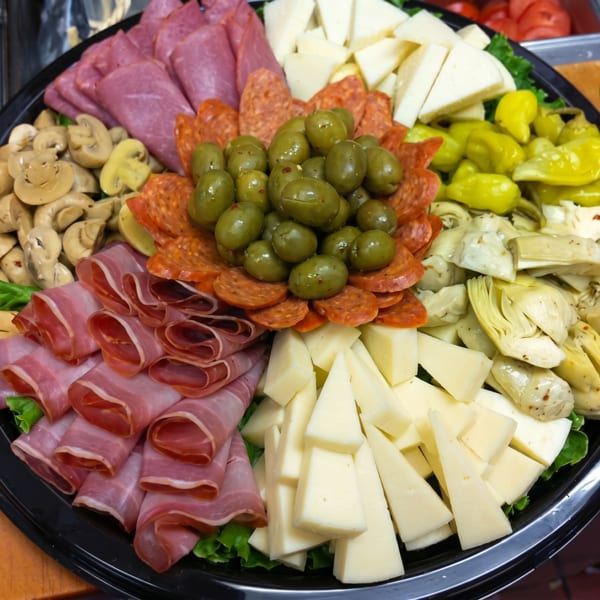 A large platter of antipasto with meats, cheeses, olives, mushrooms, artichokes, and peppers.