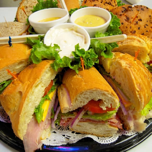 A platter of various submarine sandwiches, garnished with lettuce and three dipping sauces.