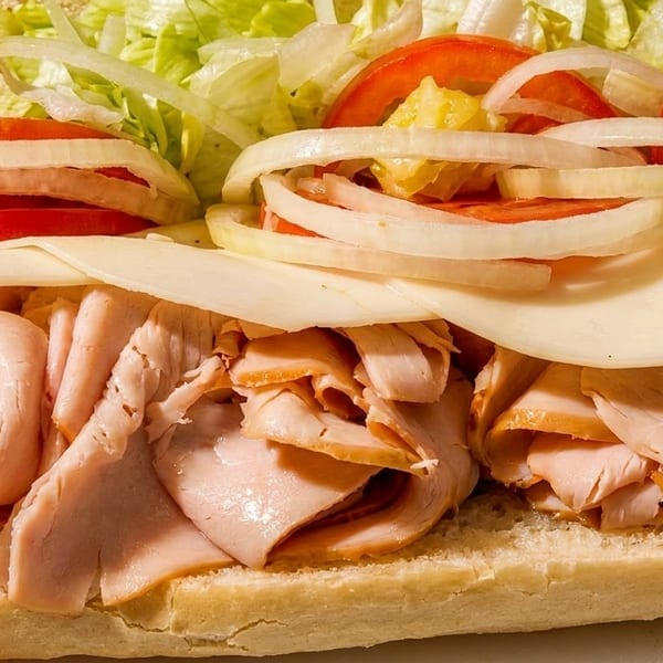 Close-up of a turkey sub sandwich with cheese, tomatoes, onions, and shredded lettuce.