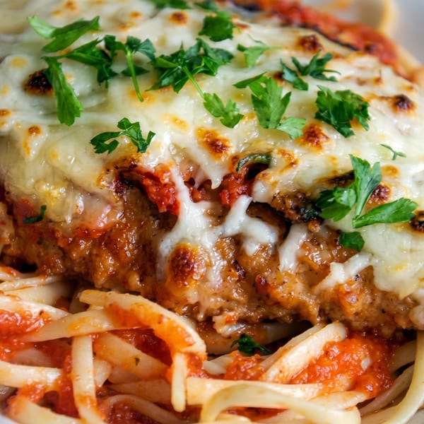 Close-up of chicken parmesan with melted cheese and parsley over linguine pasta with red sauce.